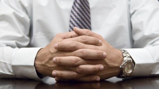 Close up of a businessman's hand clasped on his desk.